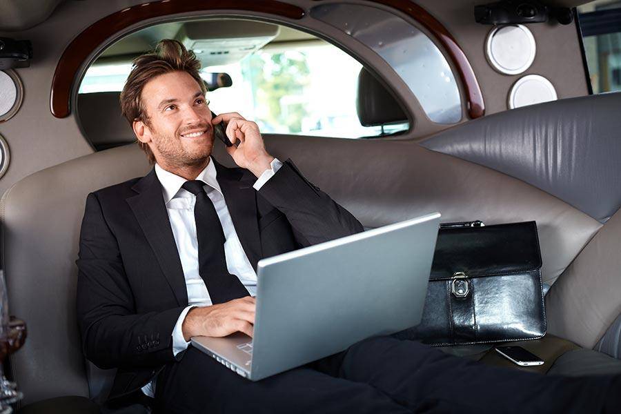 Corporate executive car service passenger working on laptop during luxury limousine transfer.