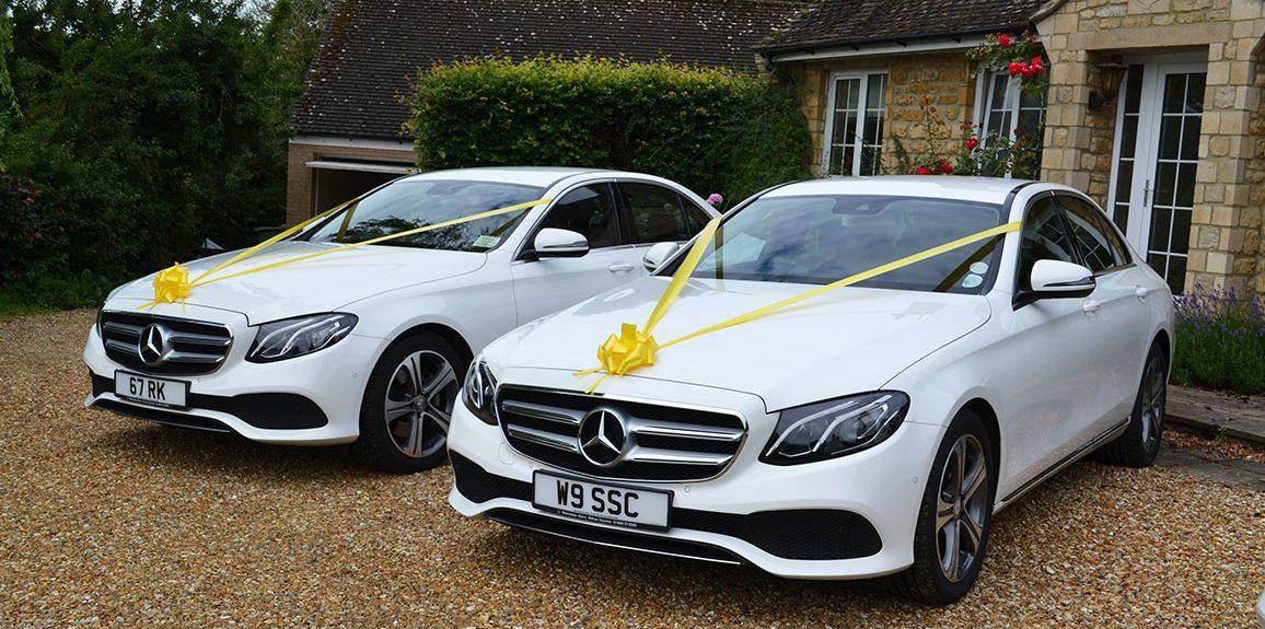 White Mercedes-Benz E-Class wedding car hire service decorated with yellow ribbons.